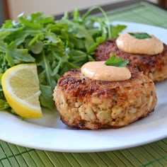 two crab cakes on a plate with greens and lemon wedges