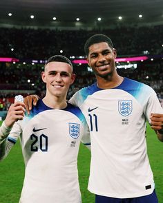 two men standing next to each other in front of a soccer field with fans watching