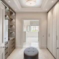 a large walk in closet with white walls and beige carpeted flooring that has a round ottoman on it