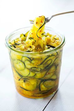 a glass jar filled with pickles and cheese on top of a white wooden table