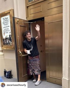 a man standing in an open door with his hand up to the camera and waving