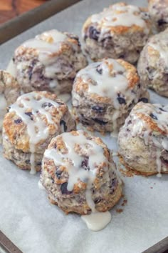 blueberry muffins with icing sitting on top of a baking sheet, ready to be eaten