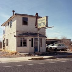 an old motel sitting on the side of a road next to a white car parked in front of it