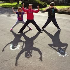 three children standing in the street with their shadows on the pavement and one child holding his hands up