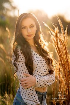 a beautiful young woman standing in a field with her arms crossed and looking at the camera