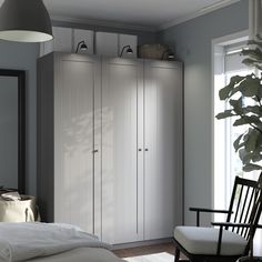 a bedroom with a bed, chair and white cupboards in front of a window