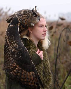 a woman is holding an owl on her head in the middle of a grassy field