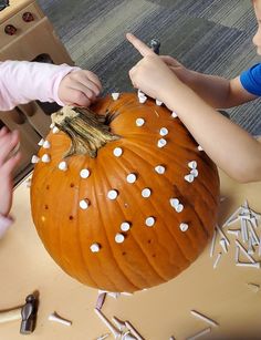 two children are carving a pumpkin with white sprinkles on it and pointing to the top