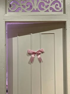 a pink bow hanging on the side of a white door with an ornate cutout