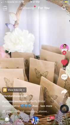 a basket filled with lots of brown paper bags next to white and pink flowers on top of a wooden table