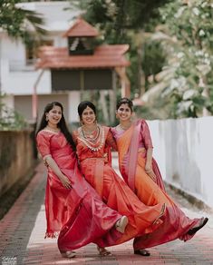 three women in red and orange saris posing for the camera on a brick walkway