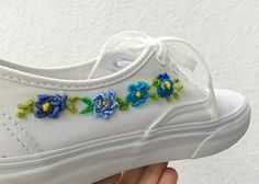 someone is holding their white tennis shoe with blue and green flowers on the laces