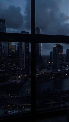 the city lights are on as seen from an office window at night, with dark clouds in the sky