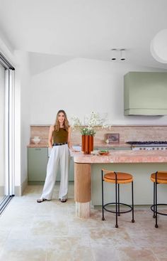 a woman standing in the middle of a kitchen next to two stools and an island