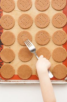 a person holding a fork over some crackers on a baking sheet with holes in it