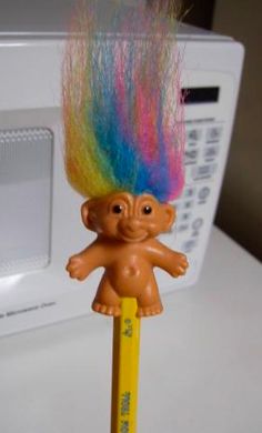 there is a small toy troll on top of a pencil in front of a microwave