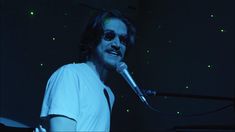 a man with sunglasses on singing into a microphone in front of a dark room filled with stars