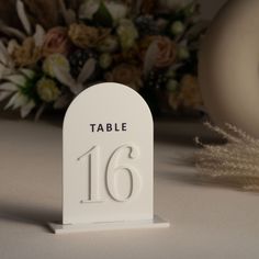 a white table number sitting on top of a table next to a bouquet of flowers