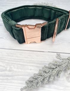 a green velvet bracelet with rose gold buckles on it, sitting on a white wooden surface