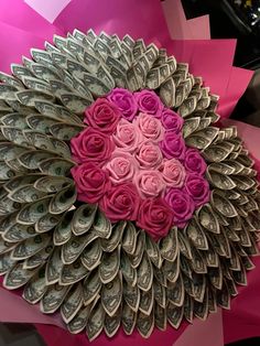 pink and purple roses are arranged in the shape of a heart made out of dollar bills