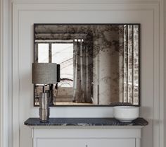 a large mirror sitting on top of a white cabinet next to a lamp and table