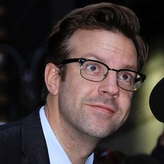 a man wearing glasses and a suit looks at the camera