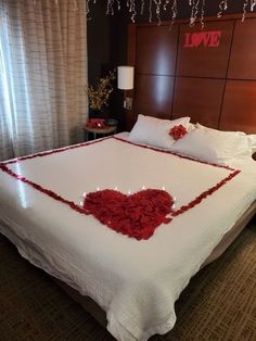 a bed with white sheets and red flowers on the headboard is decorated with hearts