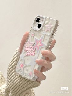 a woman holding up her phone case with stars on the front and back, while she is wearing a white sweater