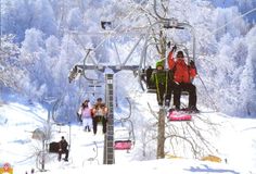 several people are riding the ski lift in the snow, while others stand on it