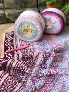 two balls of yarn sitting on top of a blanket next to a potted plant