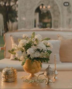 white flowers in a gold vase on a table with other decorations and decorating items