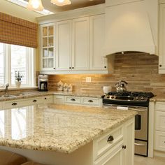 a kitchen with white cabinets and marble counter tops