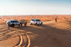 three vehicles parked in the desert with people standing around them and sand dunes behind them