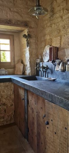 a rustic kitchen with stone walls and wooden cabinets is pictured in this image, there are dishes on the counter