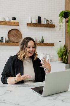 a woman sitting at a table with a laptop in front of her and talking to someone