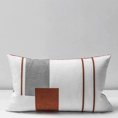 a white and brown striped pillow on a grey background with an orange square in the middle