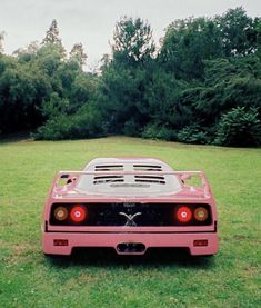 a pink car parked on top of a lush green field next to trees and bushes