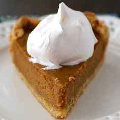 a slice of pumpkin pie with whipped cream on top sits on a white plate, ready to be eaten