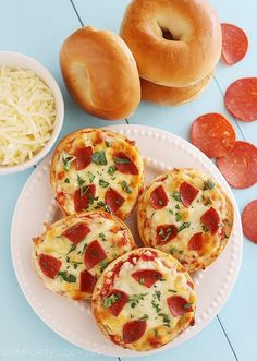 four mini pizzas on a white plate with cheese and pepperoni in the background