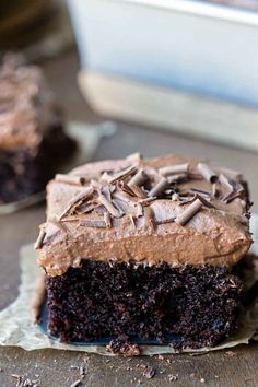 a piece of chocolate cake with frosting and sprinkles sitting on wax paper