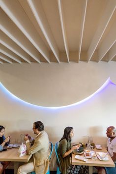 people sitting at tables in a restaurant with white walls and circular lights on the ceiling