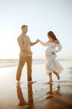 a man and woman dancing on the beach at sunset with their hands in each other's pockets