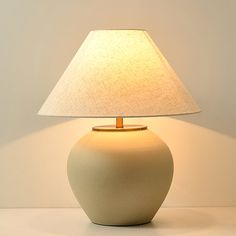 a white table lamp with a beige shade on it's base and a light in the middle