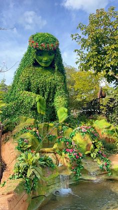 a garden with plants and water features a statue of a woman's head surrounded by greenery