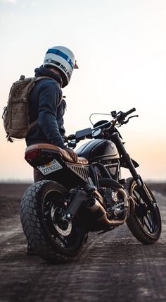 a man sitting on top of a motorcycle with a backpack strapped to the back of it