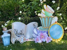 an open book sitting on top of a lush green field next to flowers and vases