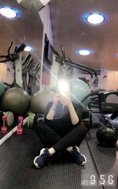 a woman sitting on the ground taking a photo with her cell phone in a gym