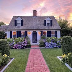 a white house with blue shutters and pink flowers in the front yard at sunset