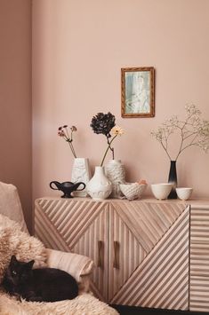 a black cat laying on top of a bed next to a dresser and vases