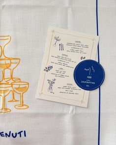 a table cloth with an embroidered menu and wine glasses on it, sitting next to a napkin